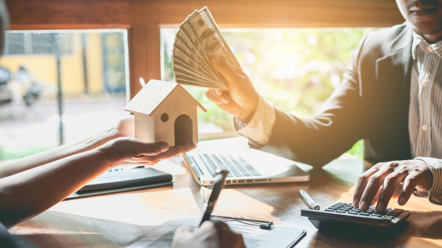 Homebuyer holding a house figurine, lender handing the borrower cash as down payment assistance to purchase a home.