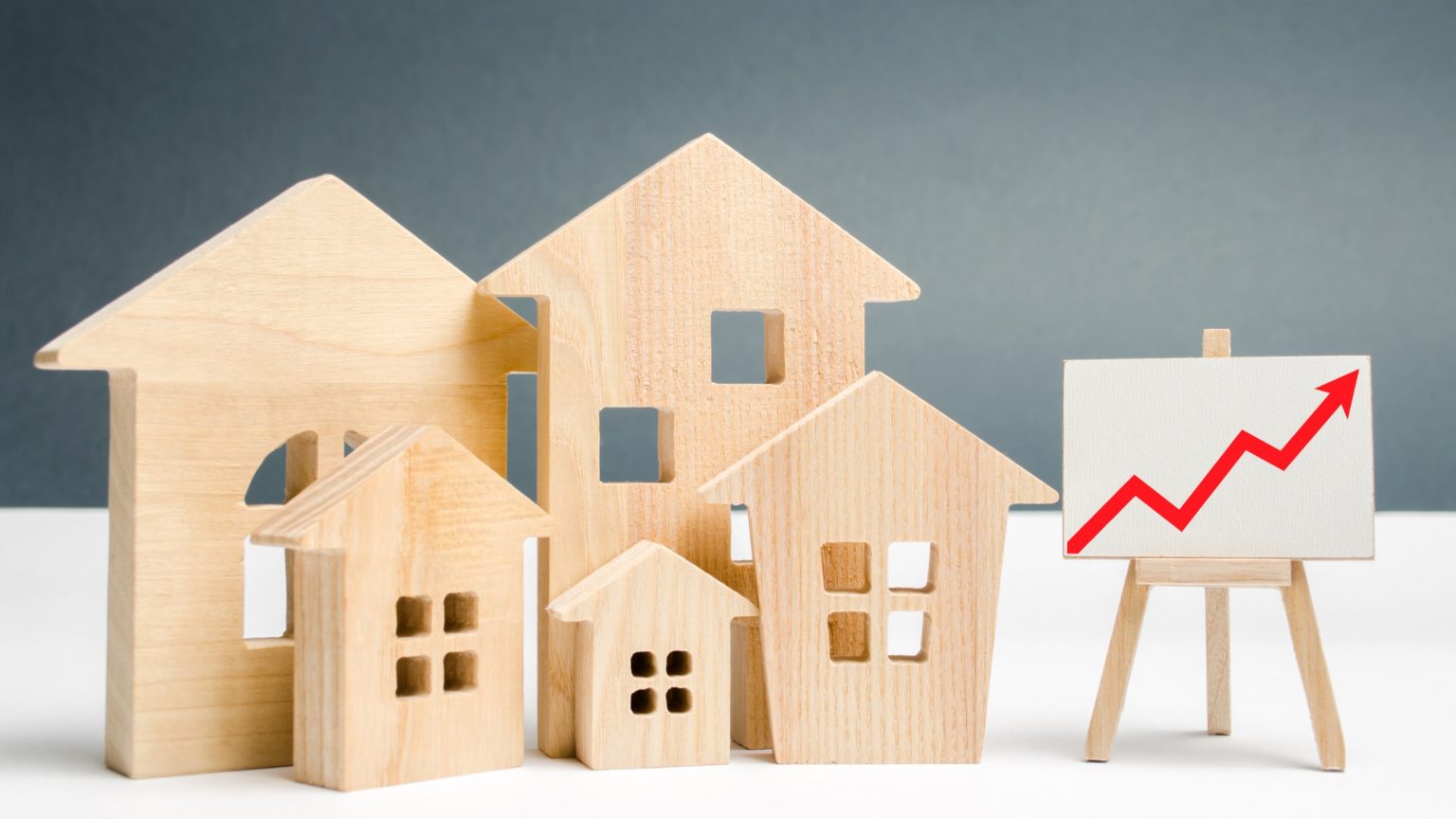 House price increases, chart showing up arrow next to wooden home figurines.
