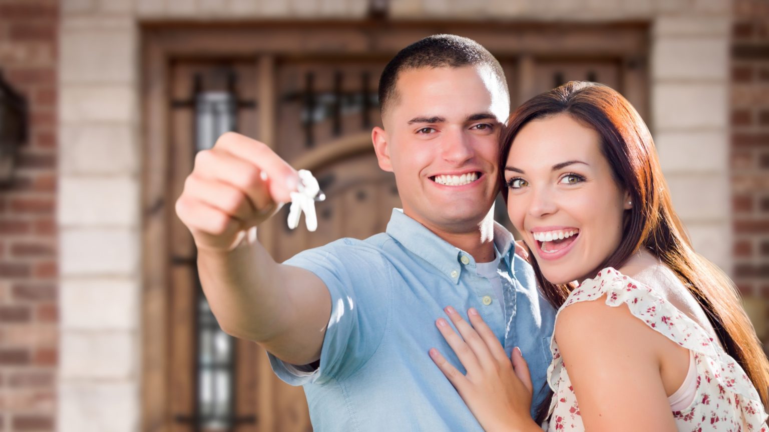 Young couple smiling, holding house keys as first-time homebuyers.