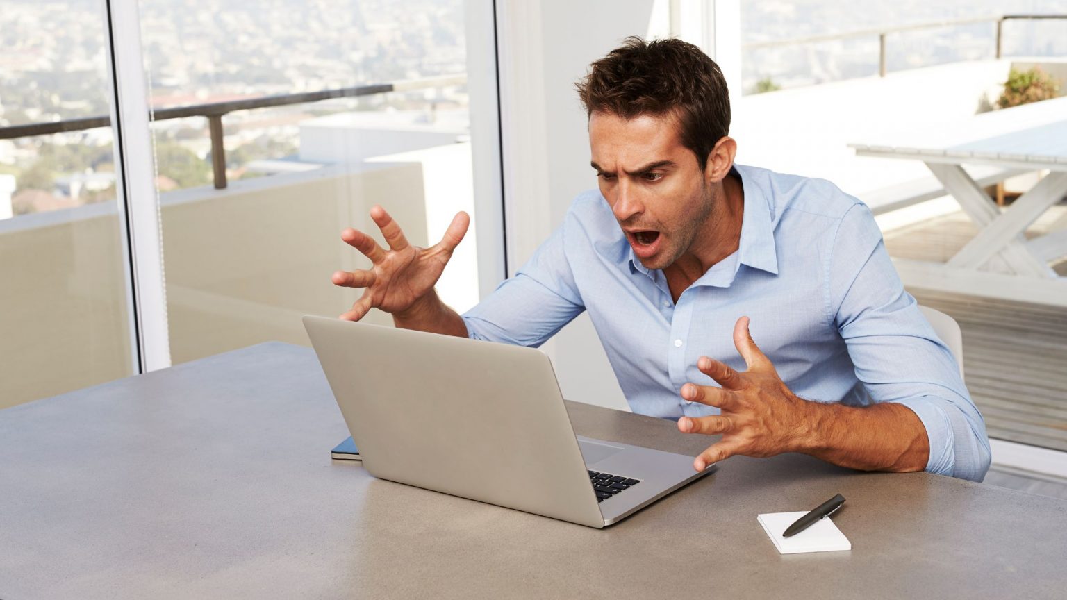 White male frustrated, looking at laptop with hands in the air, look of disbelief on his face.