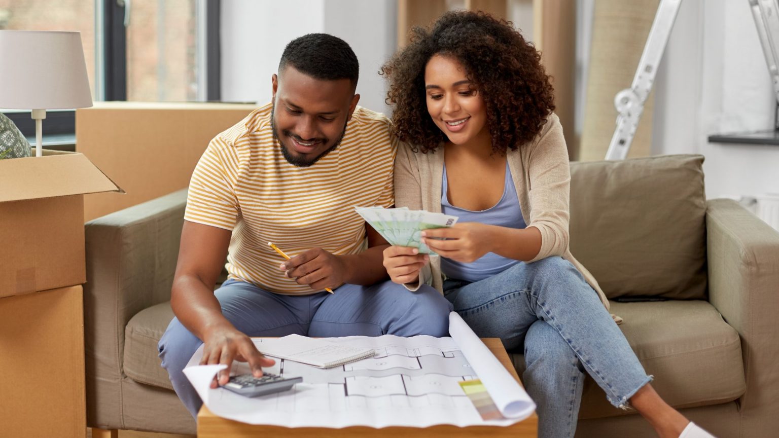 Young couple looking at house blueprints and holding cash from a refinance to perform home improvements.