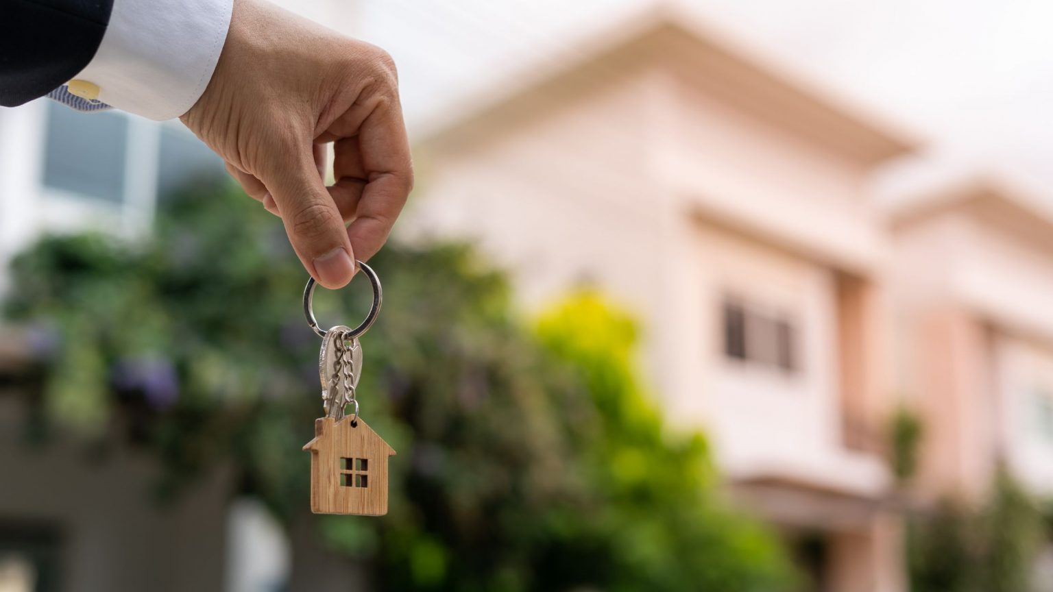Homebuyer showing house keys in front of luxury jumbo real estate.