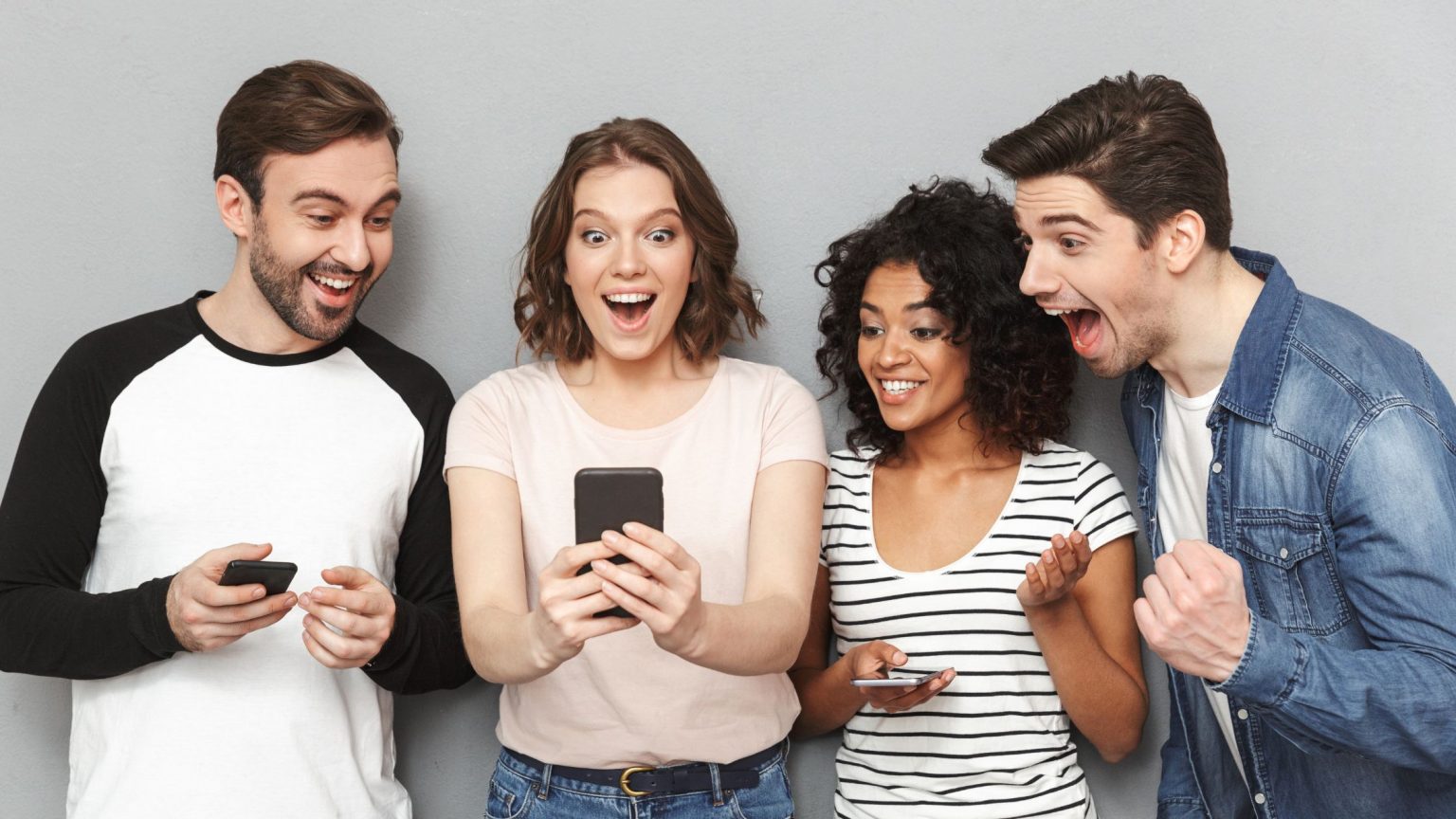Two young males and two young females looking at the young females phone, excited and smiling.
