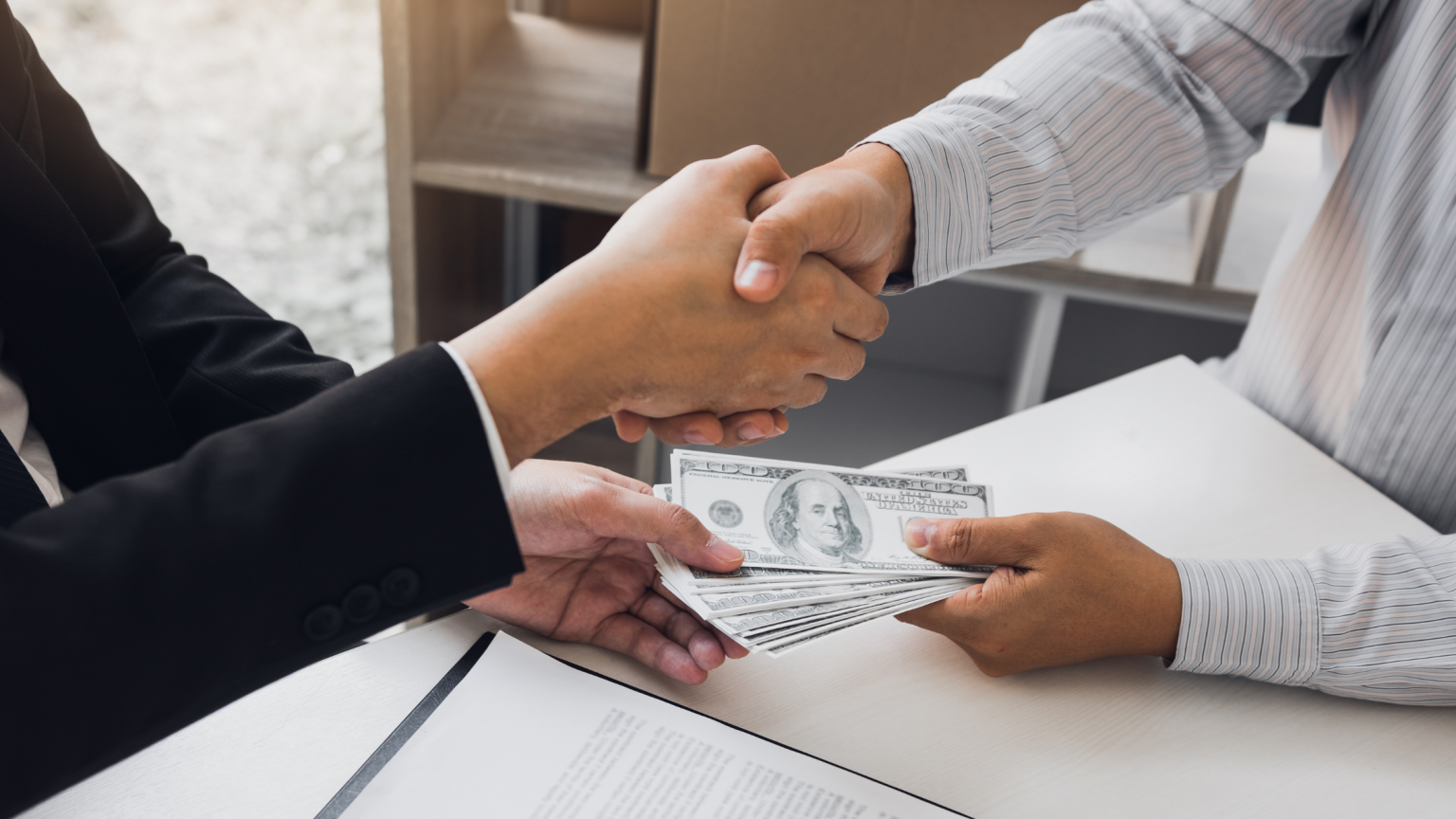 Man and woman shaking hands handing each other cash in other hand over table.