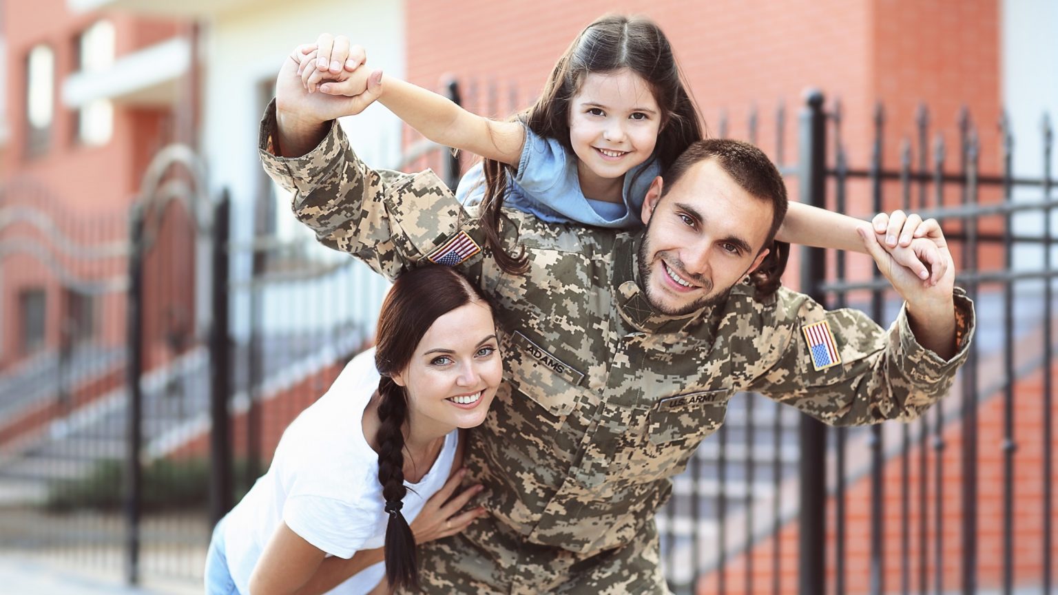 Military family, young daughter on father's back, mother and wife smiling with family.