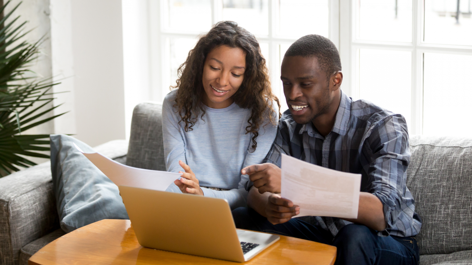 Young couple holding documents, smiling looking at computer.