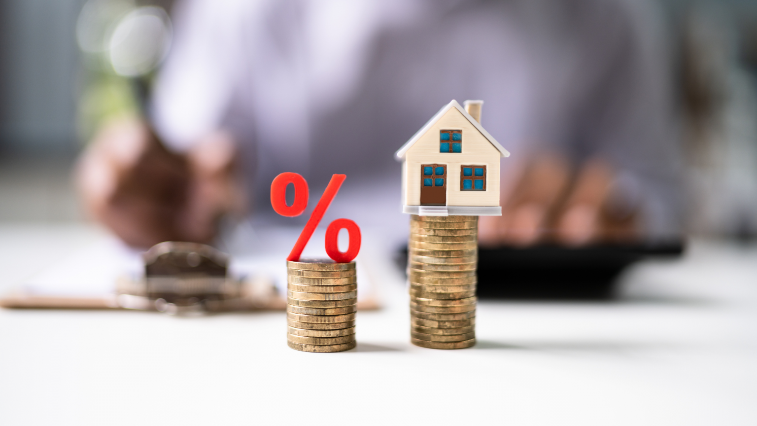 House and percentage symbol figurines sitting on stacks of coins.