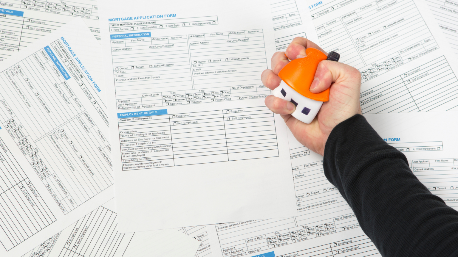 Man squeezing house stressball over mortgage applications laid out on table.