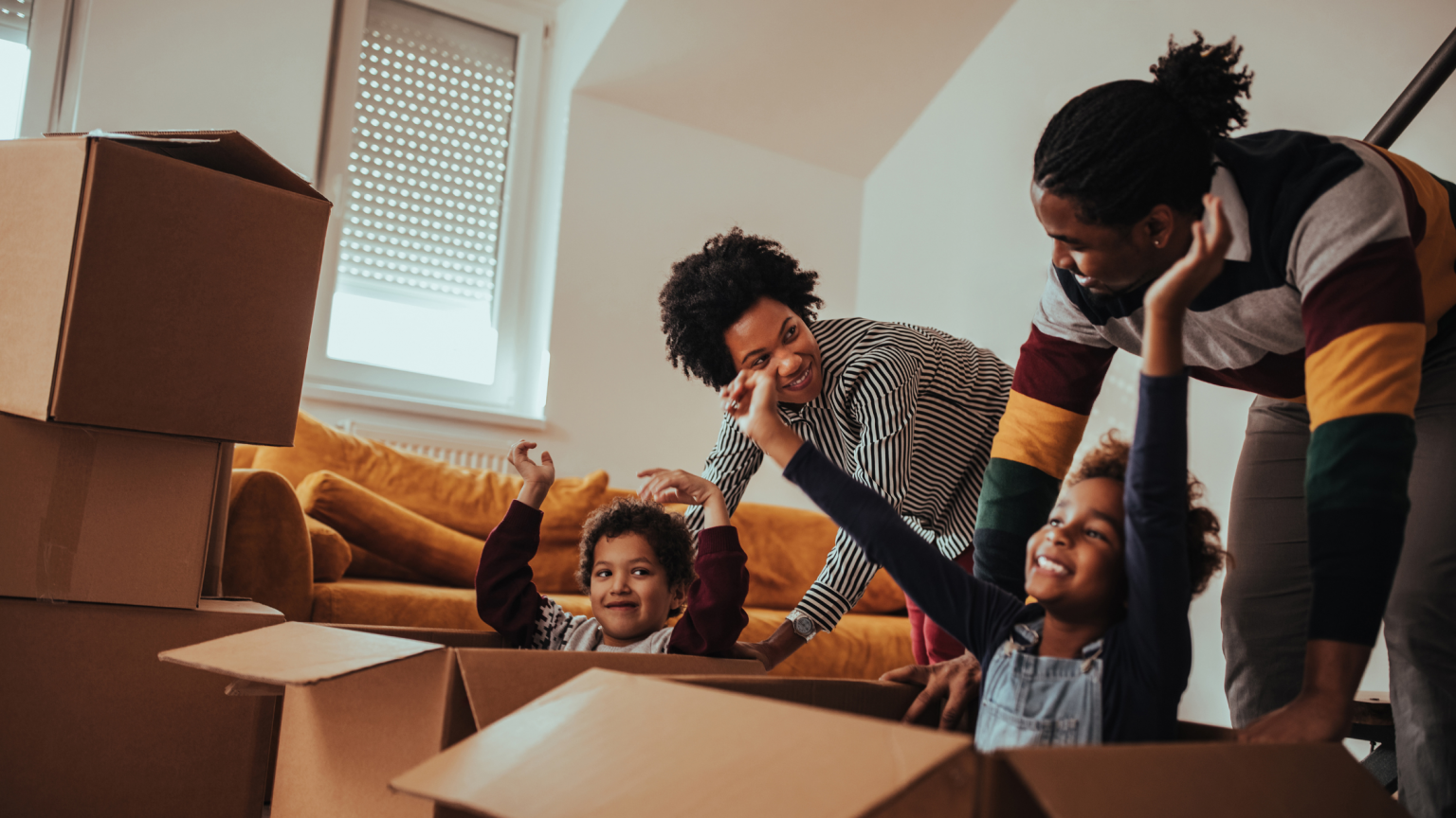 Adult couple pushing two children in moving boxes.