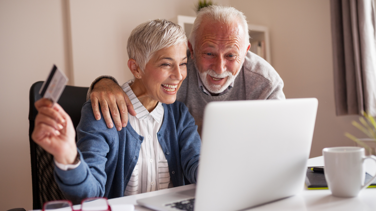 Older couple looking at laptop, woman holding credit card and smiling.