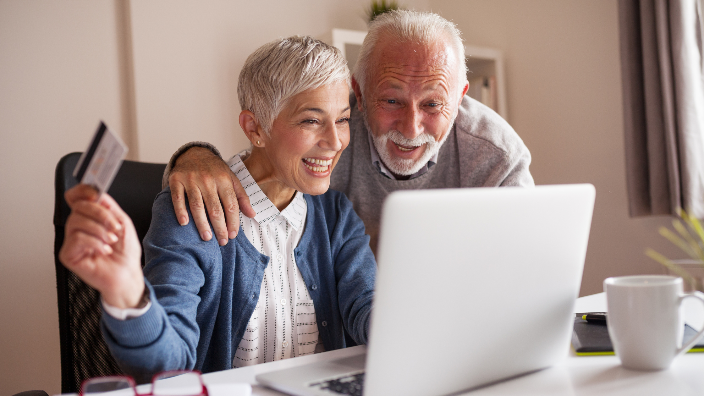 Older couple looking at laptop, woman holding credit card and smiling.