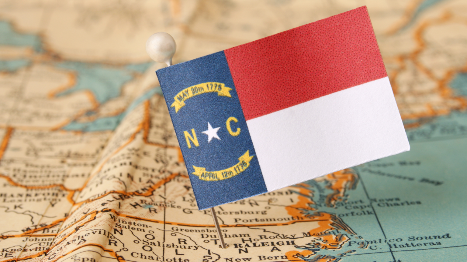NC state flag pinned on United States map in the spot of North Carolina.